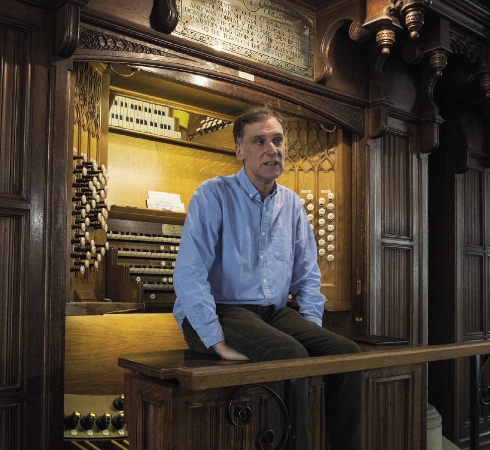 Organist Darius Battiwalla sat on the stool of the organ in Rochdale Town Hall, looking out into the hall with his back to the keyboards and stops.